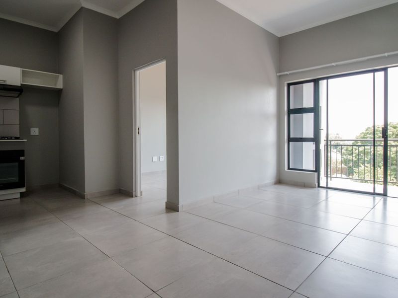 An open-plan living area featuring a modern kitchen with built-in appliances, neutral tiled flooring, and a sliding door leading to a private balcony.