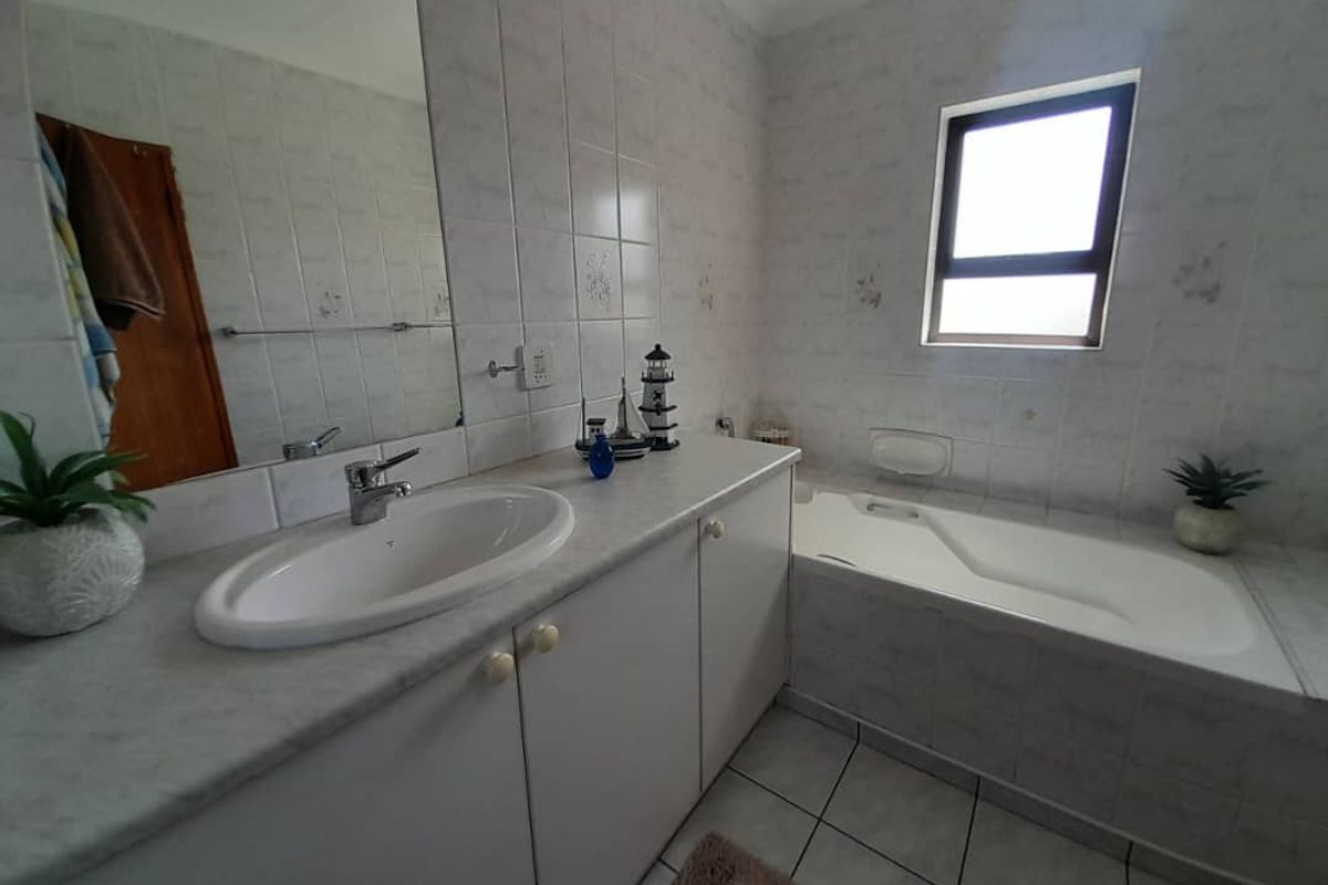 A functional bathroom featuring a built-in vanity with basin, a tiled bathtub, and neutral wall tiling throughout.