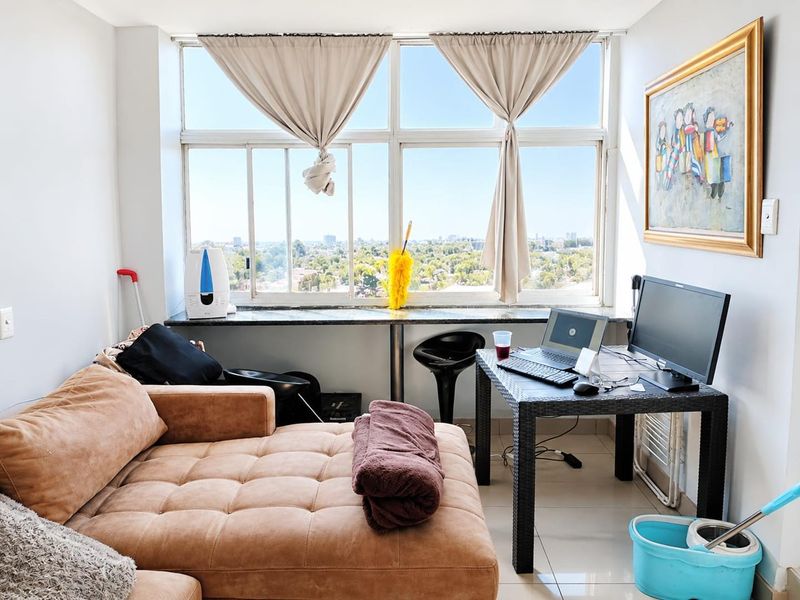 A bright living area featuring large windows with expansive city views, tiled flooring, and a built-in granite window sill.