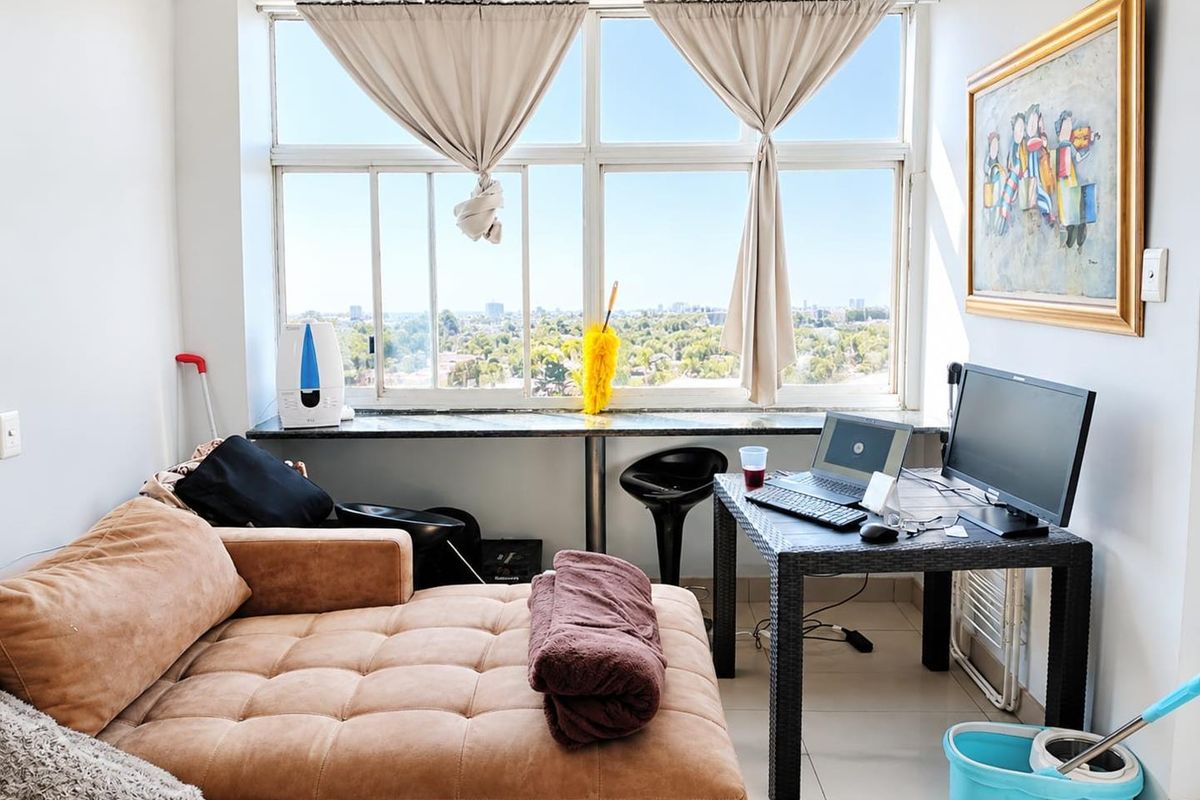 A bright living area featuring large windows with expansive city views, tiled flooring, and a built-in granite window sill.