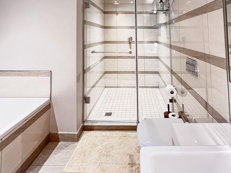 Modern bathroom featuring a built-in bathtub, separate glass-enclosed shower, wall-mounted toilet, and vanity basin with neutral tiled finishes.