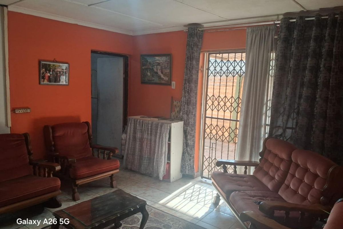 A living room featuring tiled flooring, ceiling panels, and a security gate leading to the exterior.