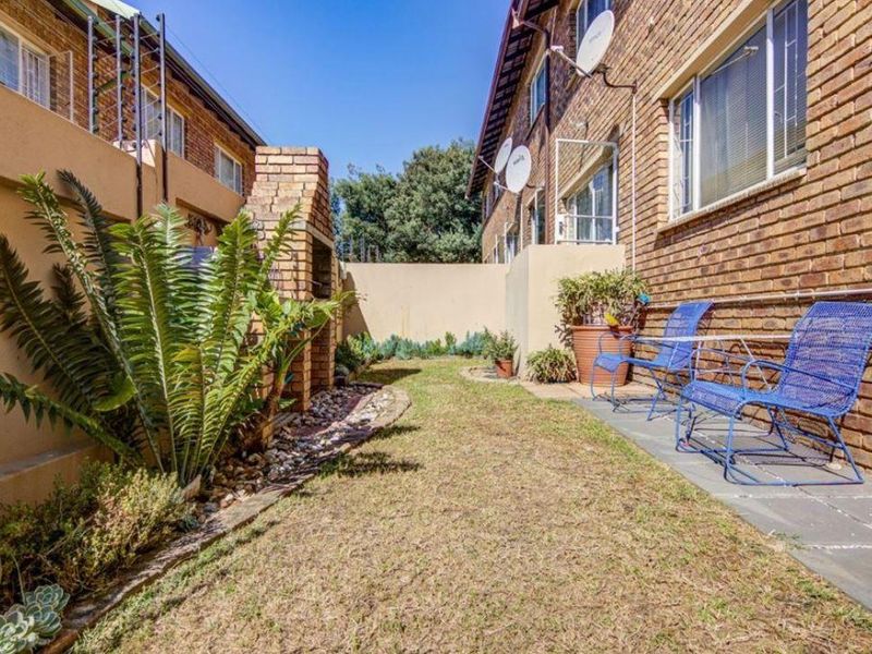 A private rear courtyard featuring a brick facade, a built-in braai, and a paved patio area adjacent to the townhouse structure.