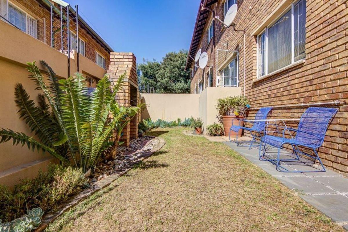 A private rear courtyard featuring a brick facade, a built-in braai, and a paved patio area adjacent to the townhouse structure.
