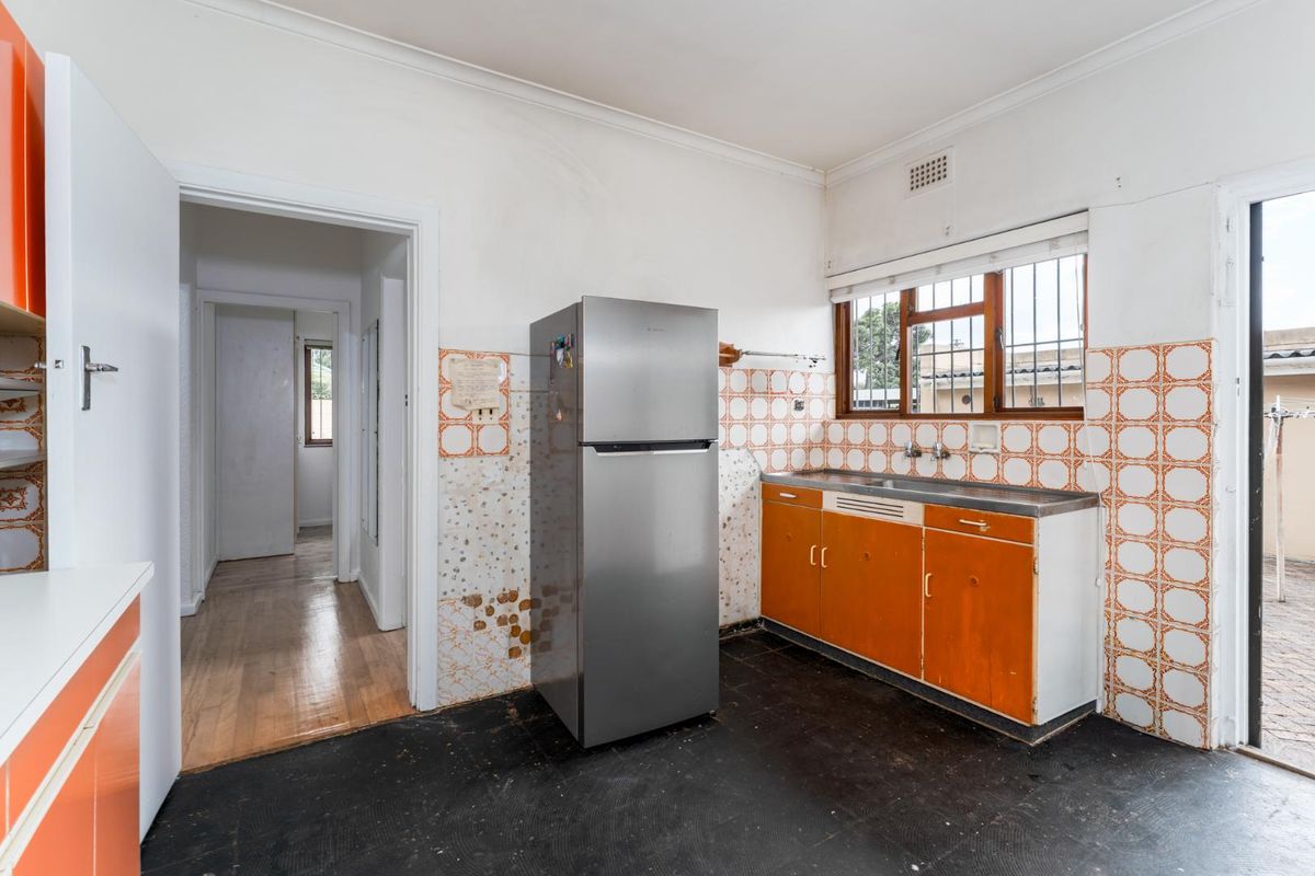 A dated kitchen featuring original orange cabinetry, a stainless steel sink, and tiled splashbacks, requiring renovation to modernize the space.