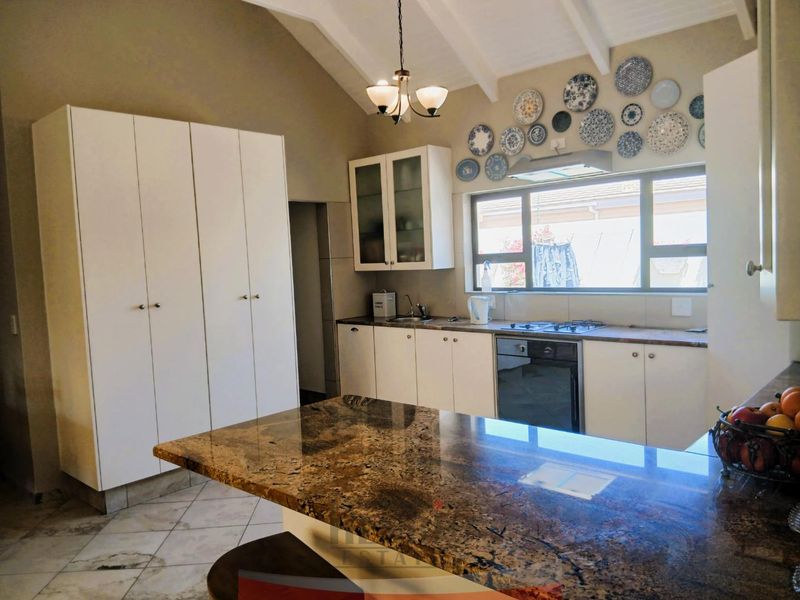 Spacious kitchen featuring granite countertops, built-in oven, gas hob, and ample cabinetry under a vaulted ceiling with tiled flooring.