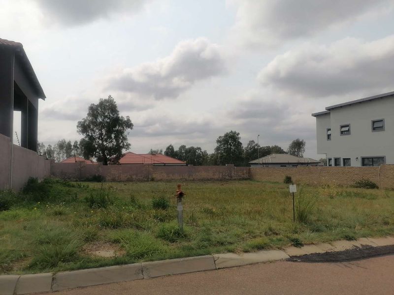 A vacant residential plot featuring a perimeter wall, fire hydrant, and street-level kerb, situated in a developed neighborhood.