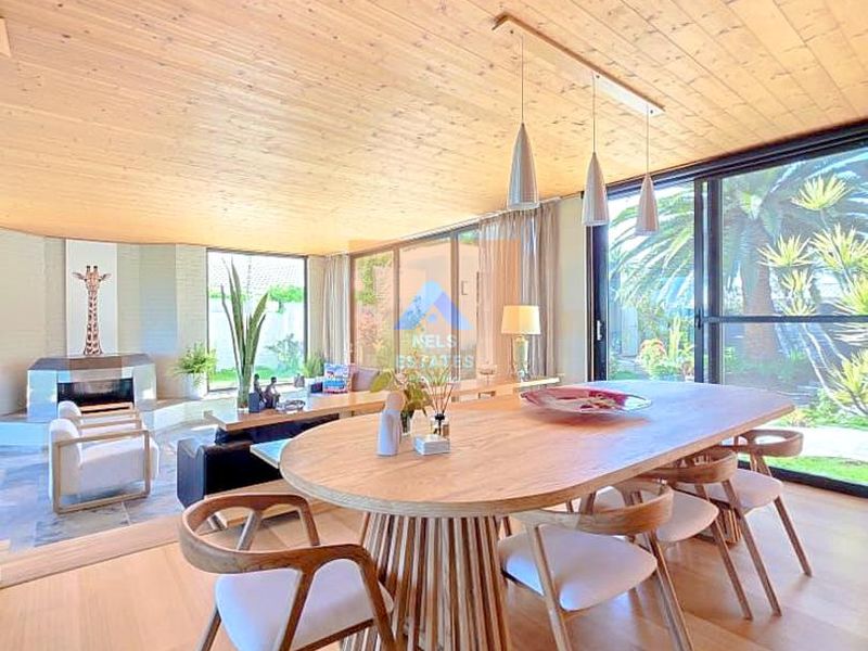 Spacious open-plan living and dining area featuring a warm timber ceiling, fireplace, and large sliding glass doors opening to the garden.