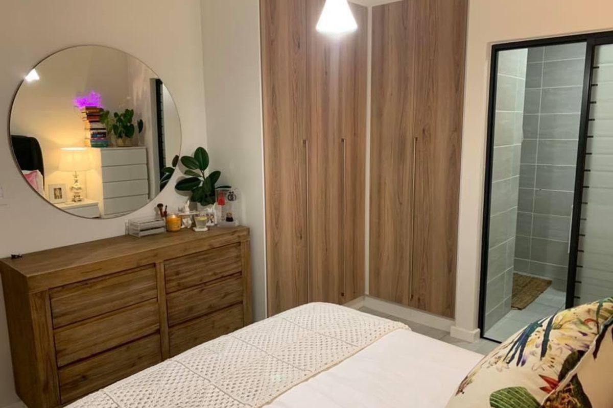 A well-maintained bedroom featuring modern wood-finish built-in cupboards, tiled flooring, and direct access to an en-suite bathroom.