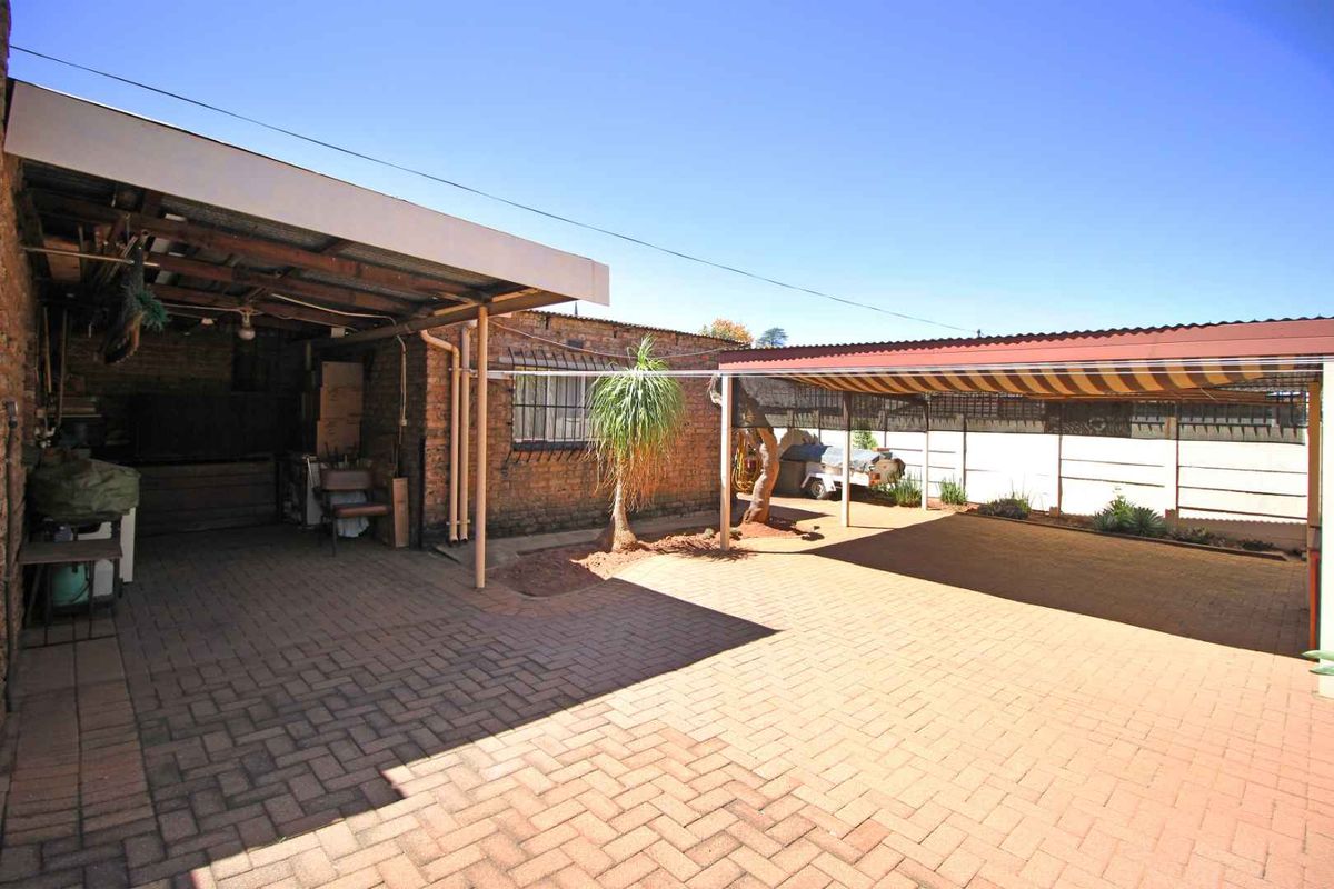 A paved outdoor courtyard area featuring a covered patio structure and additional carport shelter, providing functional space for parking or outdoor activities.