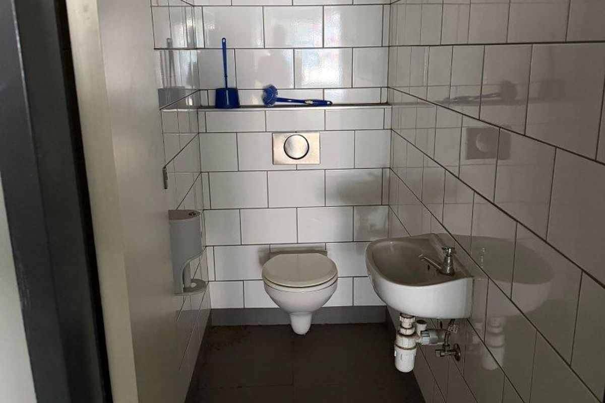 A compact restroom featuring white subway wall tiles, a wall-mounted toilet with a flush plate, and a small wall-hung basin.