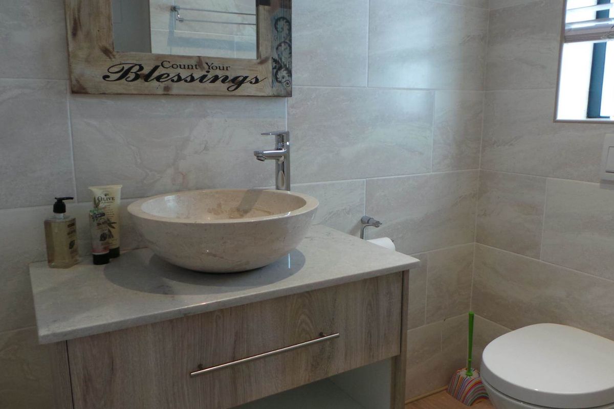 Modern bathroom featuring a stone vessel sink, vanity cabinet, wall-mounted toilet, and neutral floor-to-ceiling wall tiles.