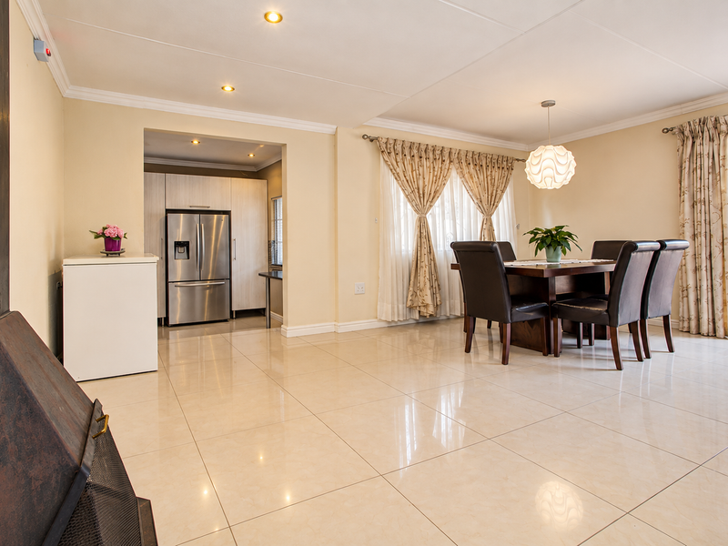 Spacious open-plan living and dining area featuring large format floor tiles, recessed lighting, and a built-in fireplace, with direct access to the outdoor patio.