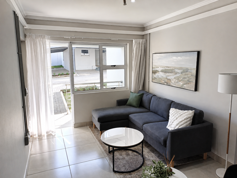A bright living room featuring neutral tiled flooring, modern cornicing, and a large sliding glass door providing access to an outdoor area.