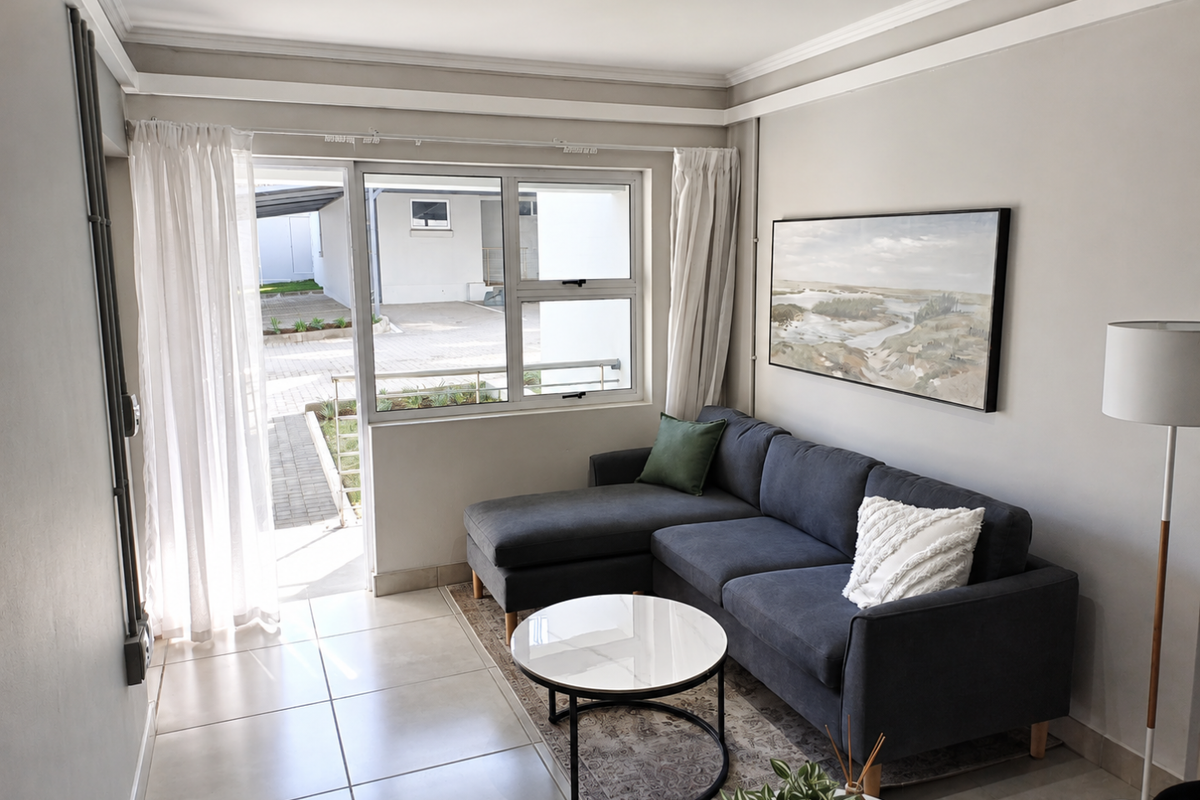 A bright living room featuring neutral tiled flooring, modern cornicing, and a large sliding glass door providing access to an outdoor area.