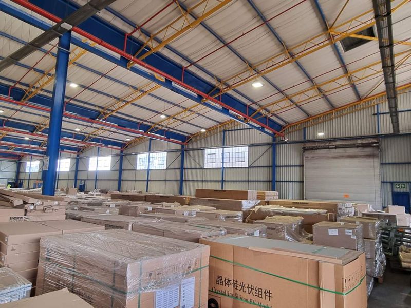 Spacious industrial warehouse featuring high-clearance steel truss roofing, exposed structural columns, and a large roller shutter door for efficient loading and access.