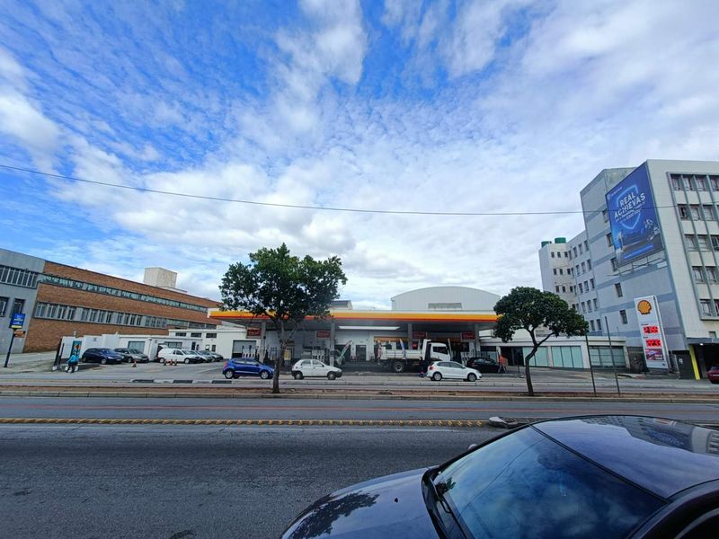 Street-level view of a commercial fuel station facility featuring a large canopy, fuel pumps, and paved forecourt area.