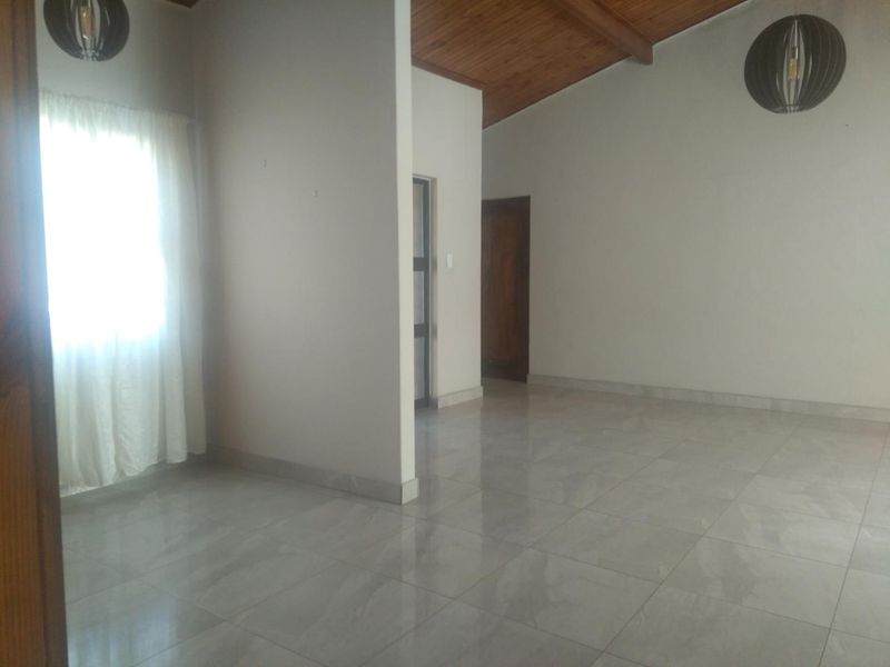 A spacious, empty living area featuring polished tiled flooring, a high exposed timber ceiling, and modern pendant lighting.