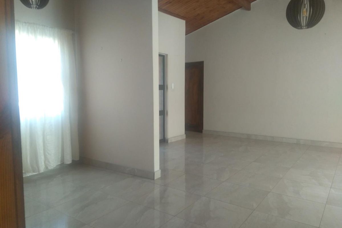 A spacious, empty living area featuring polished tiled flooring, a high exposed timber ceiling, and modern pendant lighting.