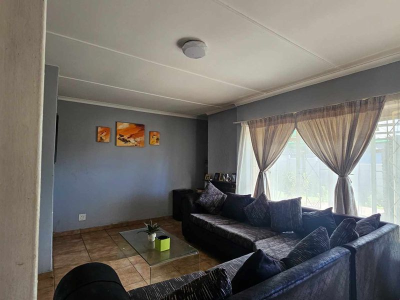 A comfortable living room featuring tiled flooring, large windows with security bars, and neutral wall tones, providing a functional and well-lit space.