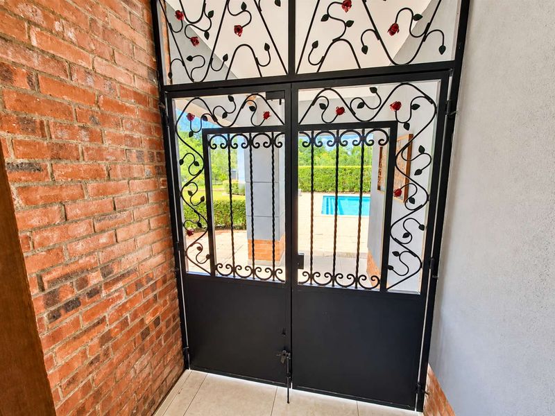 A covered patio area featuring a decorative wrought iron security gate, exposed brick wall, and tiled flooring, overlooking a swimming pool.