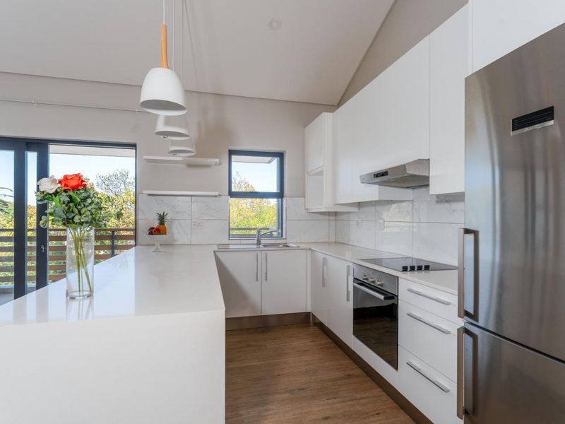 Modern kitchen featuring white cabinetry, stone countertops, integrated appliances, and a marble-look backsplash, with direct access to an outdoor balcony.