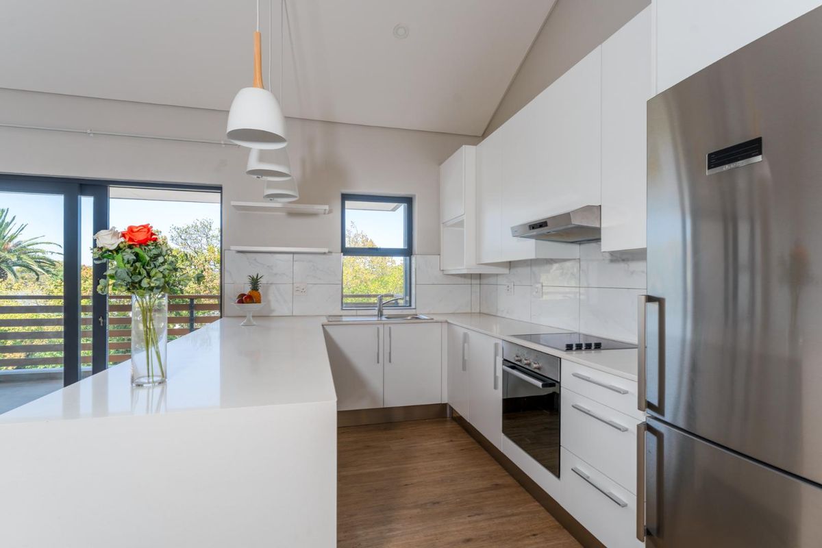 Modern kitchen featuring white cabinetry, stone countertops, integrated appliances, and a marble-look backsplash, with direct access to an outdoor balcony.