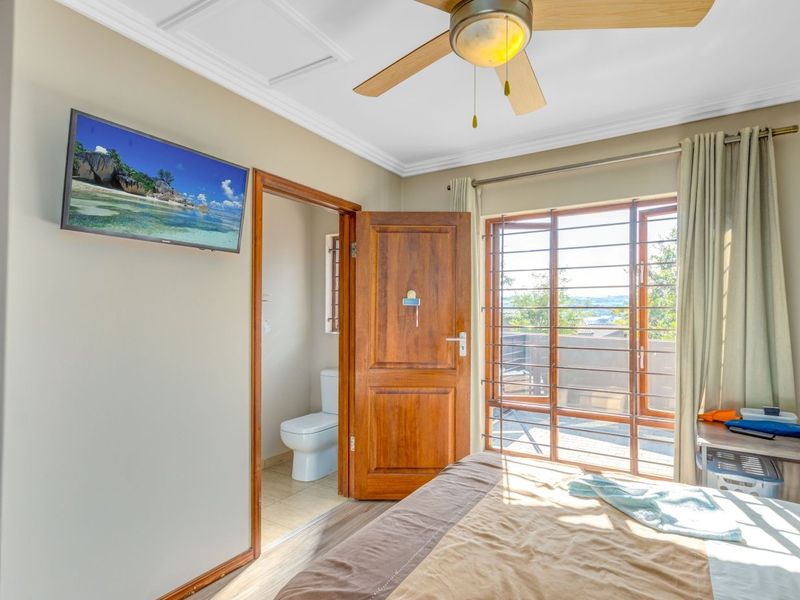 A well-maintained bedroom featuring a ceiling fan, crown molding, laminate flooring, and direct access to an en-suite bathroom and outdoor area.