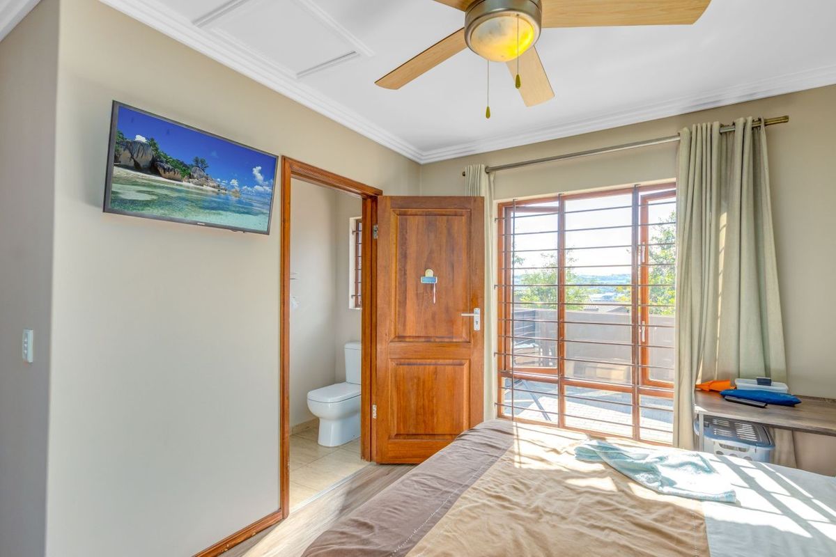 A well-maintained bedroom featuring a ceiling fan, crown molding, laminate flooring, and direct access to an en-suite bathroom and outdoor area.
