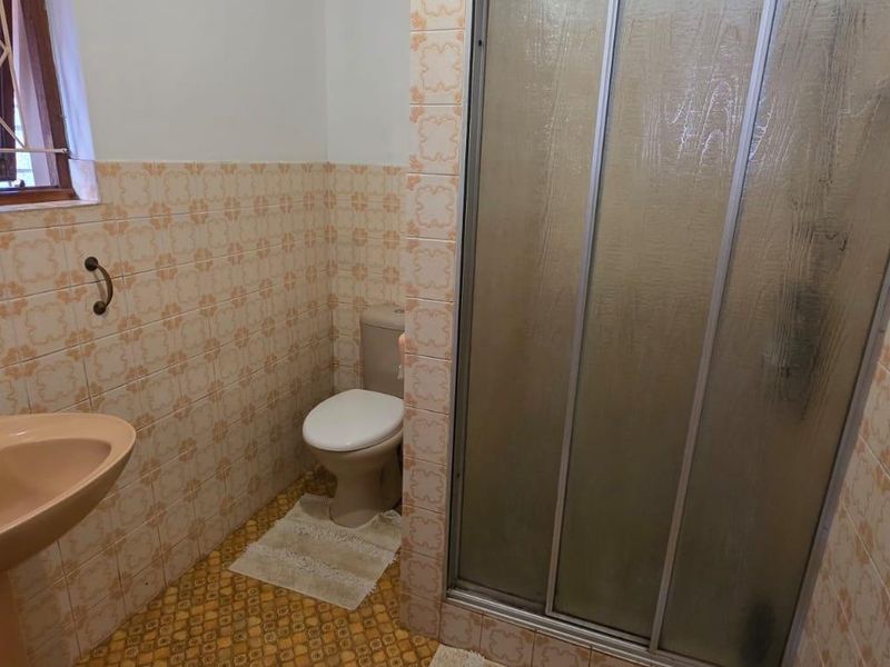 A dated bathroom featuring a pedestal basin, toilet, and a shower enclosure with sliding doors, finished with patterned wall and floor tiles.