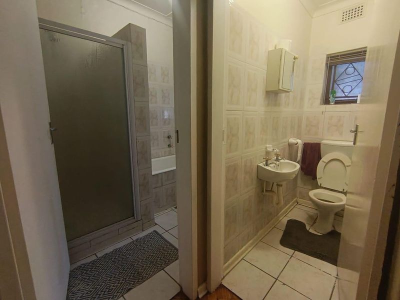 A dated bathroom featuring a separate shower enclosure, bathtub, wall-mounted basin, and toilet with tiled finishes throughout.