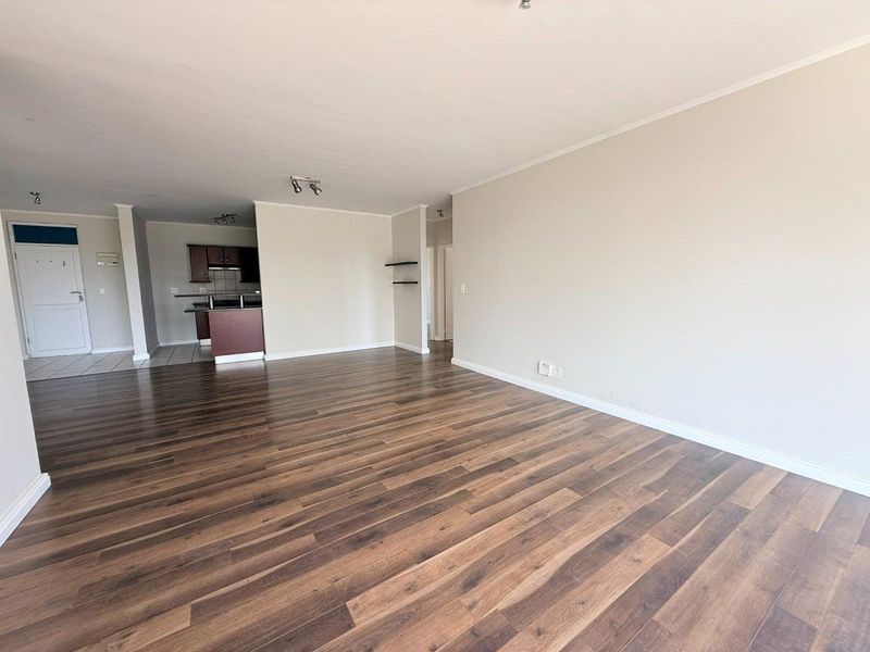 Spacious open-plan living area featuring modern laminate flooring, neutral walls, and an integrated kitchen with breakfast bar.