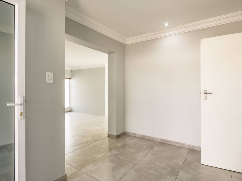 A bright and neutral entrance hallway featuring modern tiled flooring, clean finishes, and recessed lighting, leading into an open-plan living area.