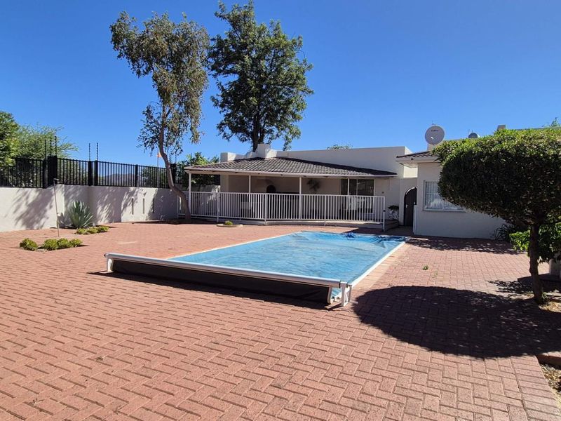 Outdoor pool area featuring a paved patio, swimming pool with cover, and a covered patio space, enclosed by boundary walls and security fencing.