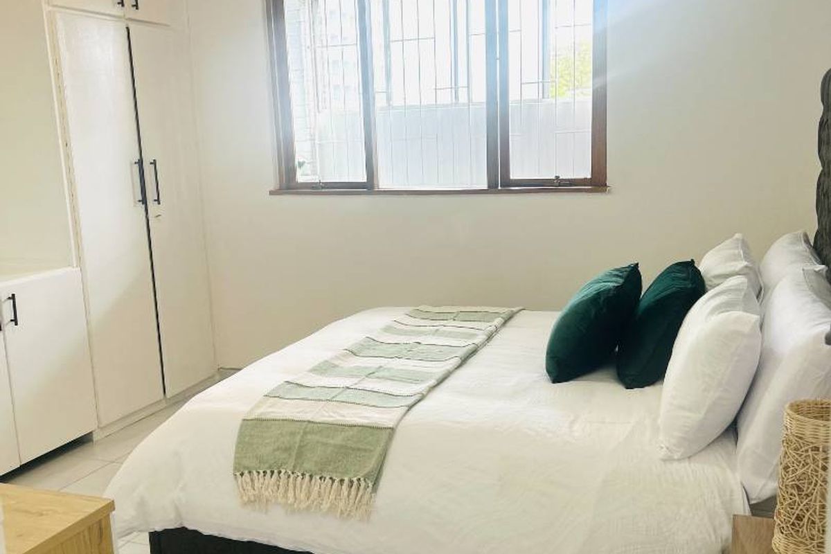 A bright bedroom featuring tiled flooring, built-in cupboards for storage, and a window fitted with security bars.
