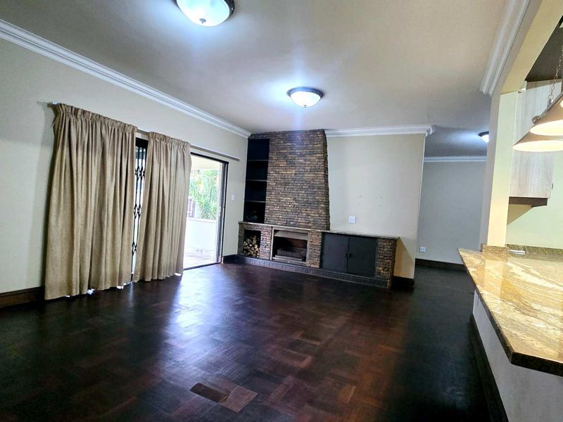Spacious open-plan living area featuring parquet flooring, a stone-clad fireplace with built-in cabinetry, and a granite breakfast bar connecting to the kitchen.