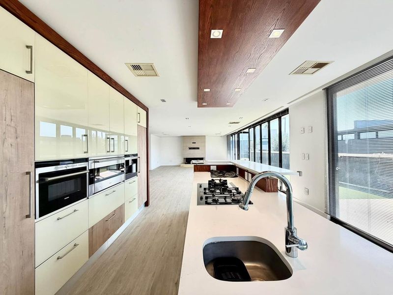 Spacious open-plan kitchen and living area featuring modern cabinetry, integrated appliances, a large island with gas cooktop, and a fireplace, leading to outdoor access.