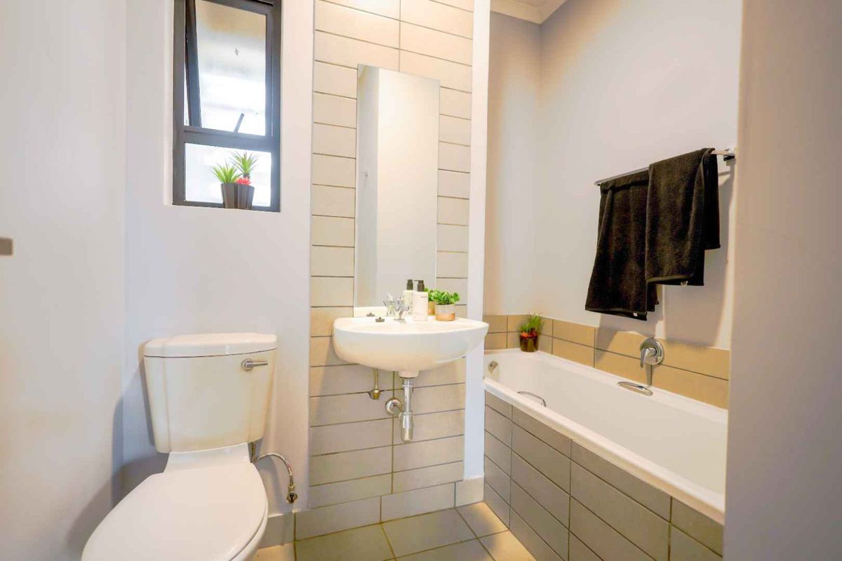 A modern bathroom featuring a wall-mounted basin, a bathtub with tiled surround, and a standard toilet.