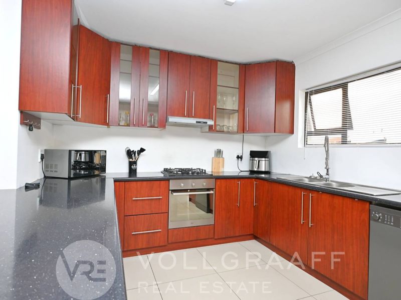 A functional kitchen featuring dark wood cabinetry, stone countertops, a gas hob, built-in oven, and integrated dishwasher.