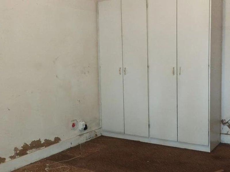 A bedroom featuring a built-in wardrobe, requiring significant cosmetic repairs to the walls and flooring to restore its condition.