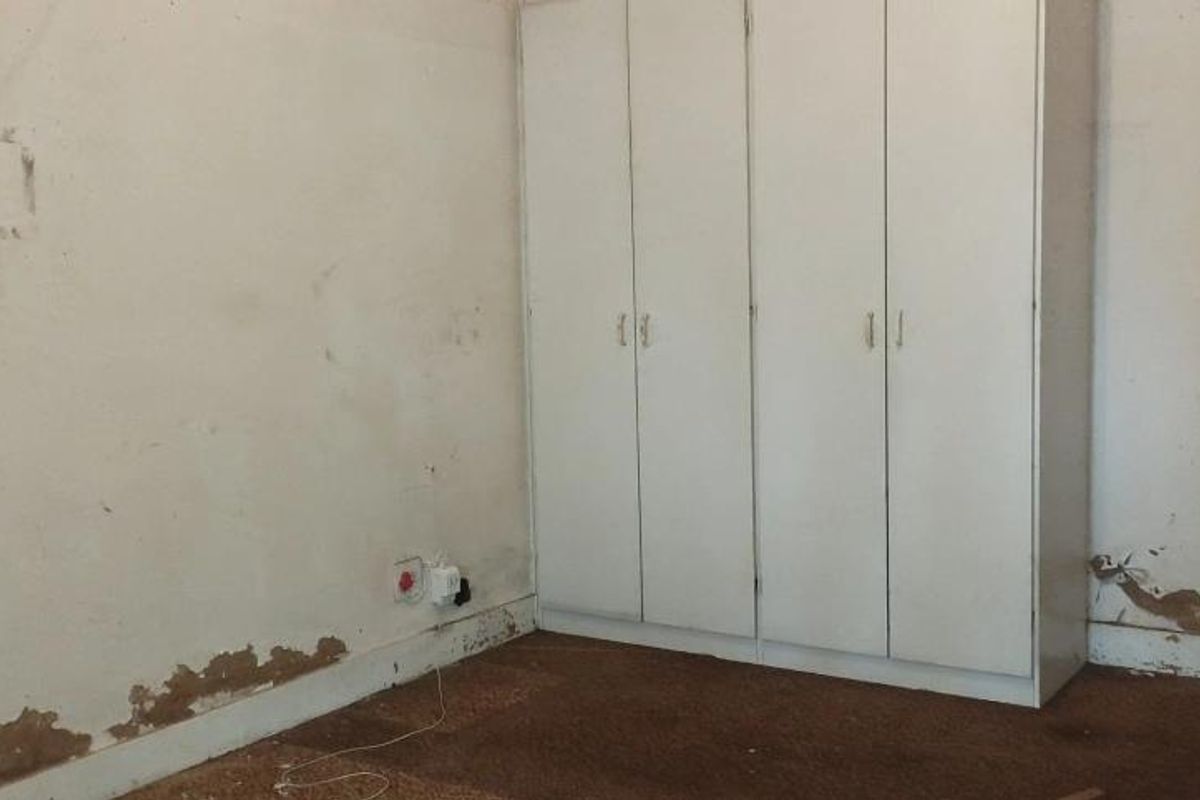A bedroom featuring a built-in wardrobe, requiring significant cosmetic repairs to the walls and flooring to restore its condition.
