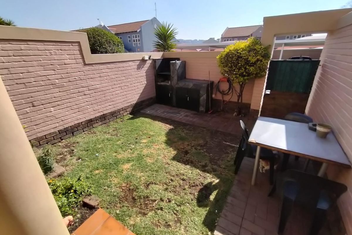 Private rear courtyard featuring a built-in braai, paved patio area, and a small lawn enclosed by brick boundary walls.