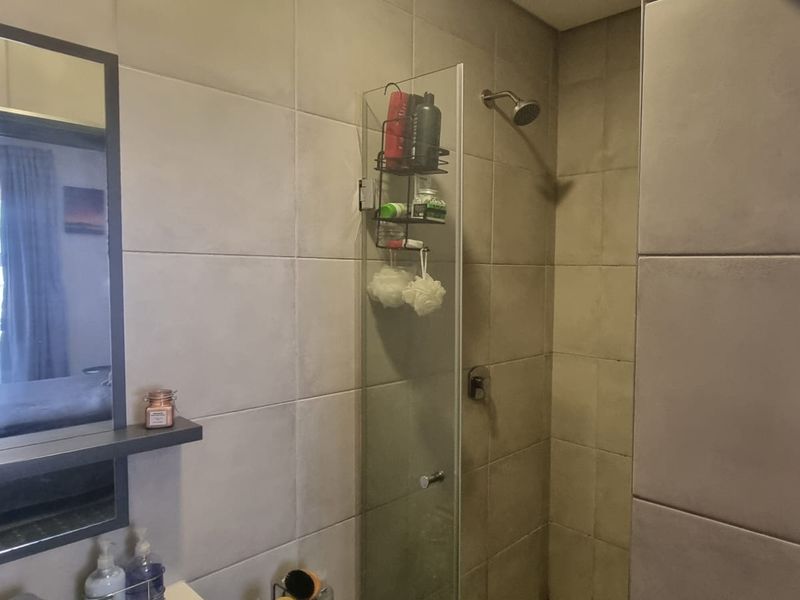 A modern bathroom featuring large format wall tiles, a glass shower enclosure with a fixed shower head, and a built-in mirror with a floating shelf.