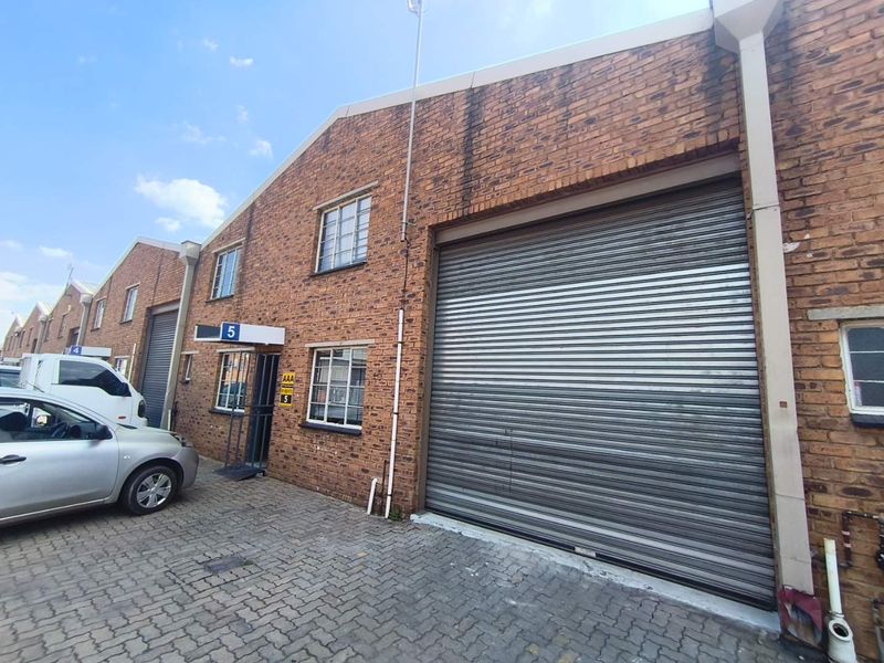 Front elevation of an industrial unit featuring a large roller shutter door, brick facade, and paved driveway access.