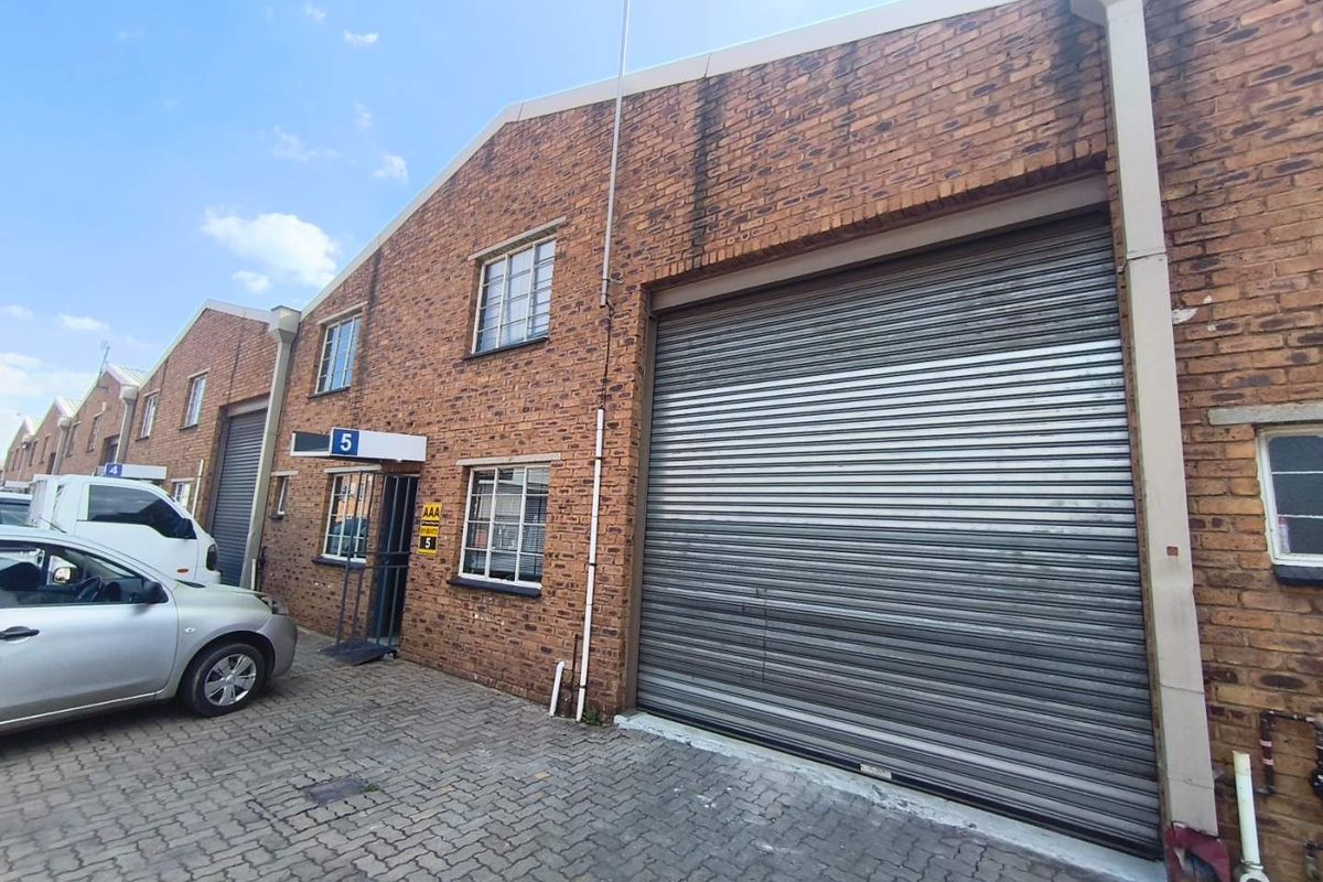 Front elevation of an industrial unit featuring a large roller shutter door, brick facade, and paved driveway access.