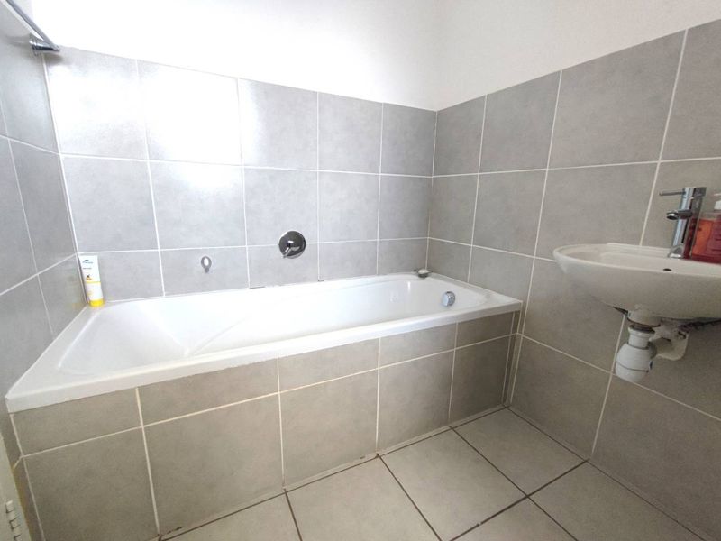 A clean, functional bathroom featuring a built-in bathtub, wall-mounted basin, and neutral grey ceramic tiling throughout.