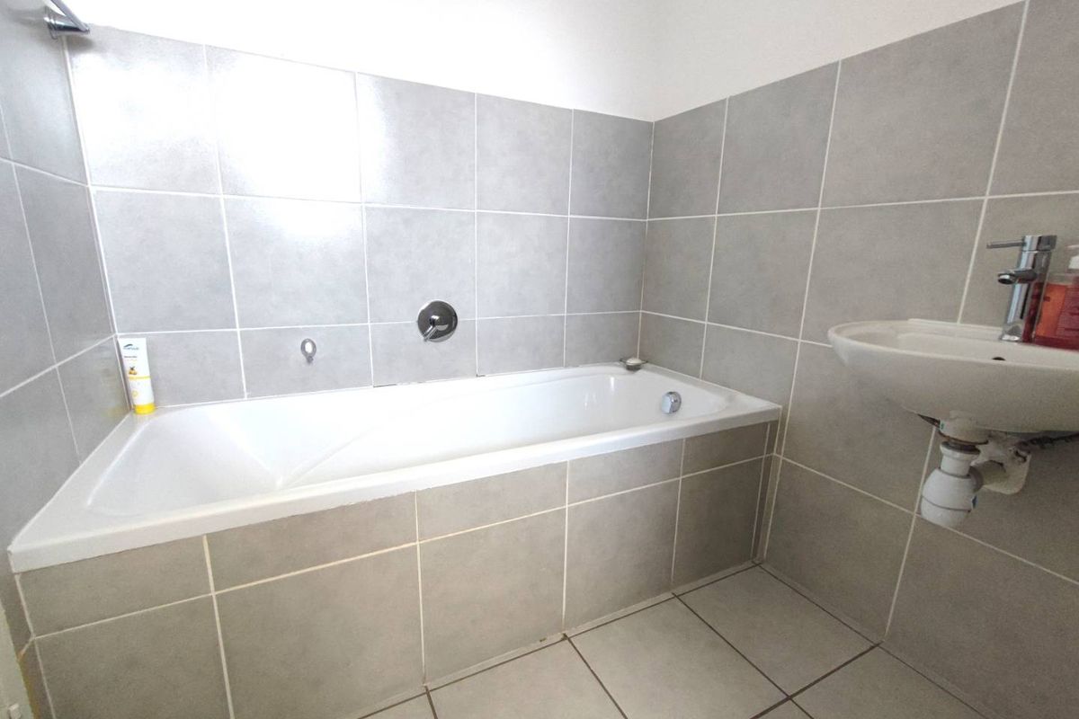 A clean, functional bathroom featuring a built-in bathtub, wall-mounted basin, and neutral grey ceramic tiling throughout.