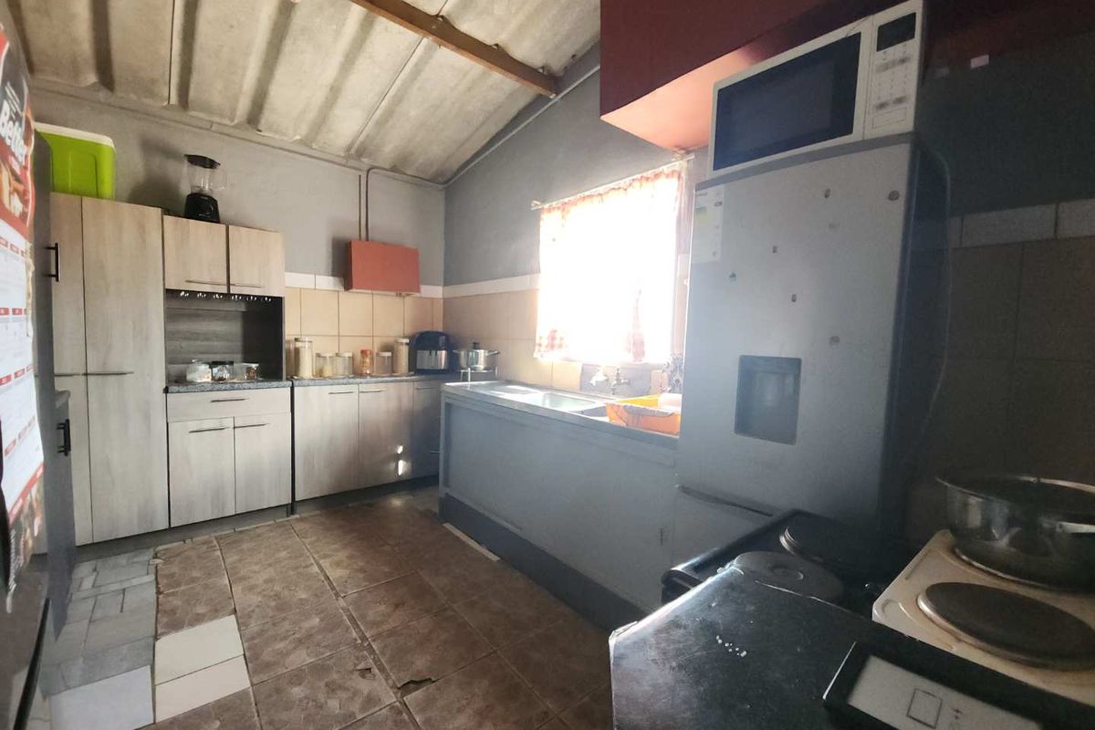 A functional kitchen space featuring built-in cabinetry, a sink area, and tiled flooring, with an exposed ceiling and dated finishes throughout.