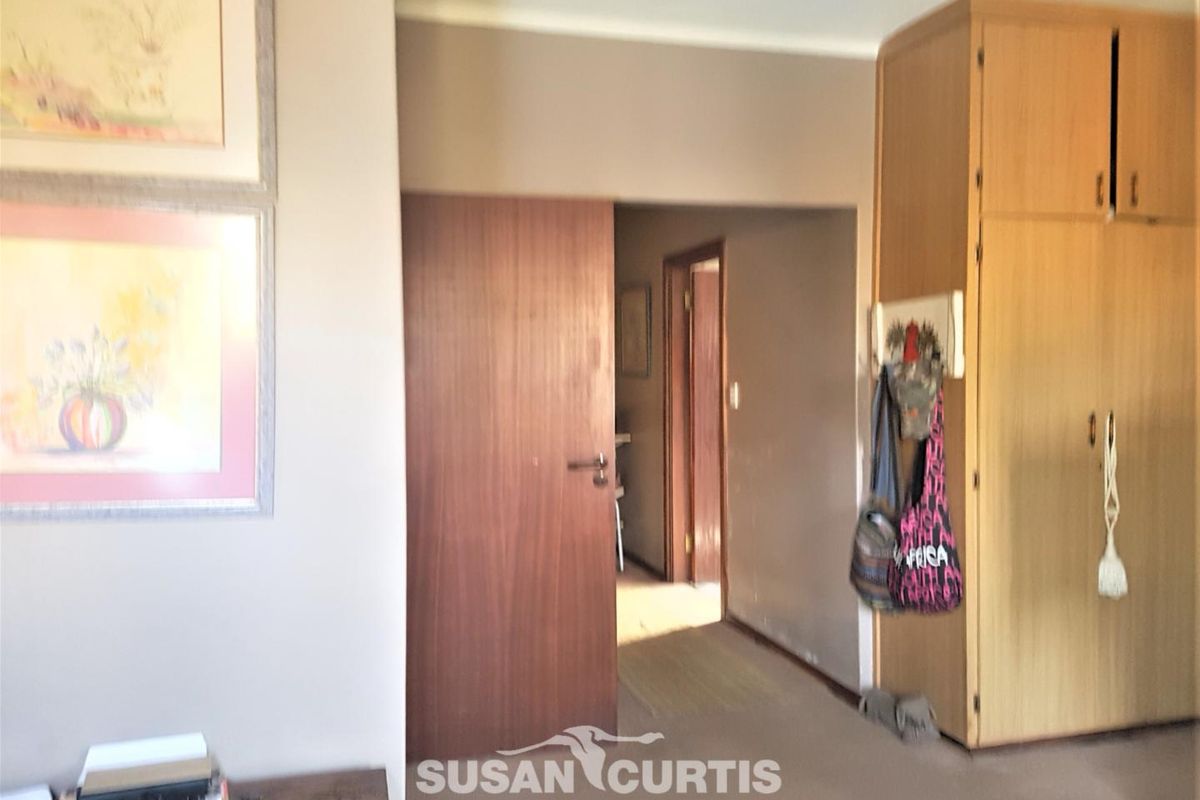 A bedroom interior featuring built-in wooden cupboards and carpeted flooring, providing access to an adjoining hallway.