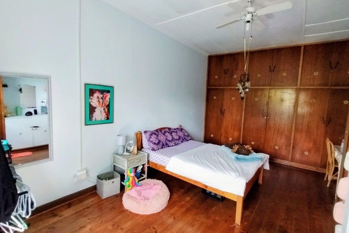 A bedroom featuring polished timber flooring, a ceiling fan, and extensive floor-to-ceiling built-in wooden wardrobes.